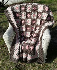 a crocheted blanket sitting on top of a chair in the grass next to a basket