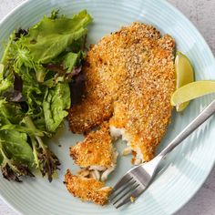 a white plate topped with chicken and salad next to a fork on top of a table