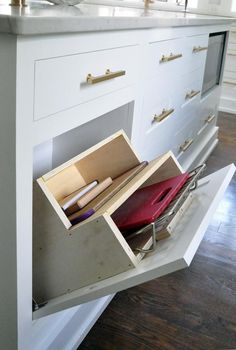 an open drawer on the side of a white kitchen counter with drawers and other items in it