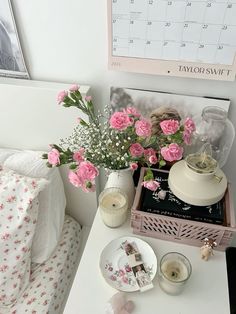 a white table topped with pink flowers next to a wall mounted calendar and candle holder