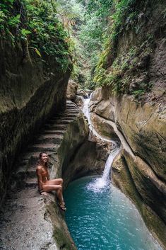 a woman sitting on the edge of a cliff next to a small pool of water