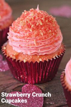 cupcakes with pink frosting and sprinkles on wooden table next to hearts