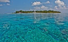 an island in the middle of the ocean with clear blue water and clouds above it