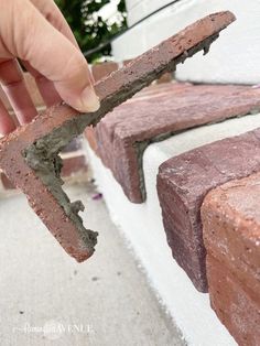 a hand holding a piece of brick on top of a cement block with one end missing