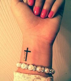 a woman's wrist with a cross tattoo on it and pearls around the wrist