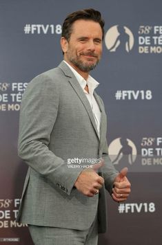 a man in a suit and white shirt smiles at the camera while standing on a red carpet