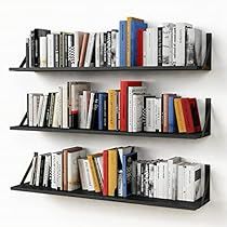 three black shelves filled with books on top of each other in front of a white wall