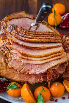 a large ham on a plate with oranges and pomegranates around it