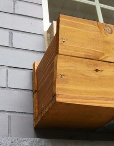 a wooden box sitting on the side of a brick building next to a window sill