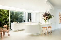 a kitchen with white counter tops and wooden stools next to a plant filled wall