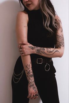 a woman with tattoos on her arms leaning against a wall