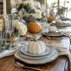 a dining room table is set with white pumpkins and silverware, greenery and candlesticks