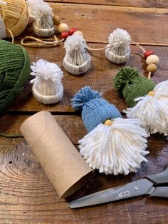 several knitted gnomes sitting on top of a wooden table next to yarn and scissors