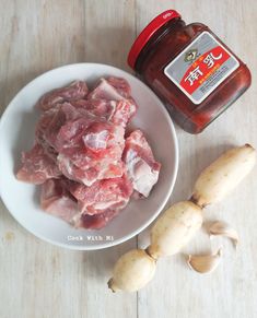 raw meat and garlic on a white plate next to a jar of hot sauce,