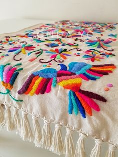 a colorful embroidered table runner with tassels and beads on it, sitting on a white surface