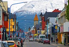 a city street with cars parked on both sides and snow covered mountains in the background