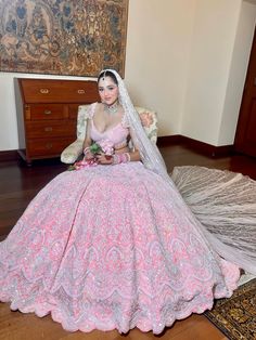 a woman in a pink wedding dress sitting on a chair with a veil over her head