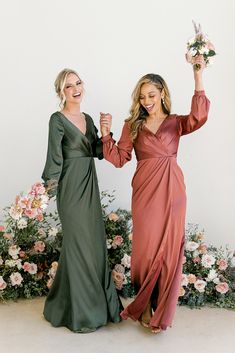 two women standing next to each other holding hands in front of flowers and greenery