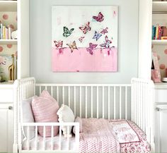 a white crib with pink and blue butterflies on the wall next to bookshelves