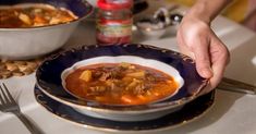 a person holding a bowl of soup on top of a table with other plates and utensils