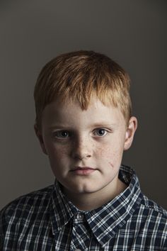 a young boy with freckled hair and blue eyes looks at the camera while wearing a plaid shirt