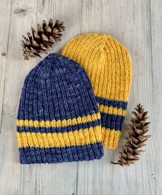 two knitted hats sitting on top of a wooden table next to some pine cones