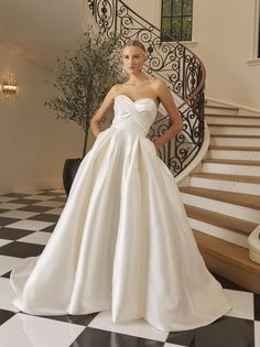 a woman standing in front of a staircase wearing a wedding dress with a bow at the waist