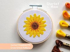 a cross stitch sunflower is next to some yarns and thread on a white surface