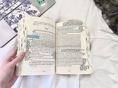 a person is reading a book while laying in bed with their laptop on the side