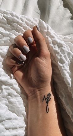 a woman's hand with a flower tattoo on her left wrist, resting on a white blanket