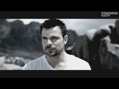 a man is standing in front of some rocks and mountains with his head tilted to the side