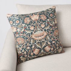 a pillow on a couch with an ornate design in blue and orange colors, sitting on the back of a chair