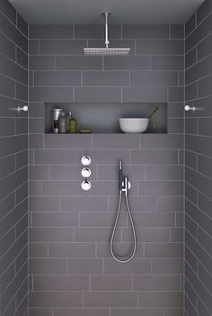 a bathroom with gray tile and white fixtures in the bathtub, shower head, and shelf