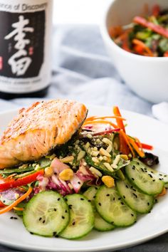 a white plate topped with fish and vegetables next to a bottle of wine on a table