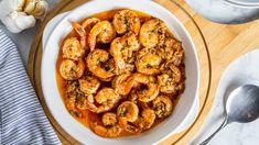 a white bowl filled with shrimp and sauce on top of a wooden cutting board next to garlic