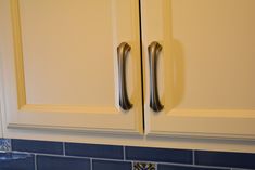 a kitchen with white cabinets and blue tile backsplash, two handles on the cabinet doors