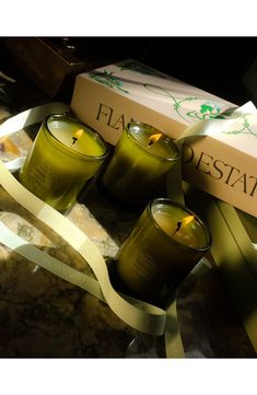 three green candles sitting on top of a table next to a box with a ribbon