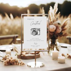 a table topped with a sign and candles next to some tall grass in front of a field