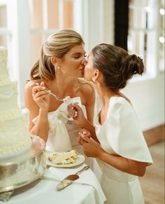 two women sharing a kiss as they eat cake at a wedding reception in the dining room