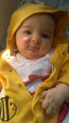 a baby in a yellow raincoat sitting on top of a bed next to a pillow