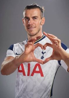 a man making a heart with his hands while standing in front of a gray background