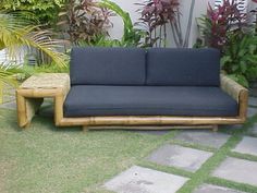 a couch sitting on top of a grass covered field next to a wooden table and plant