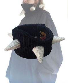 a woman holding a black and white knitted hat with horns attached to it's side