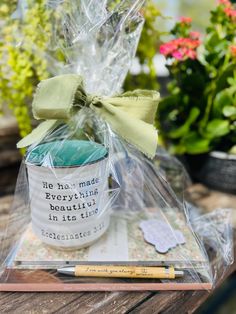 a coffee mug with a green bow on it sitting in a clear plastic bag next to some potted plants