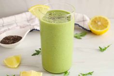 a green smoothie in a glass with lemons and chives on the side