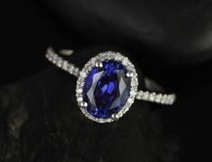 an oval shaped blue and white diamond ring on top of a black rock with diamonds around it