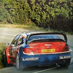 a blue and red car driving down a road next to trees on the side of a hill