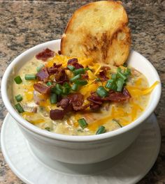 a bowl of soup with bacon, cheese and green onions next to a piece of bread