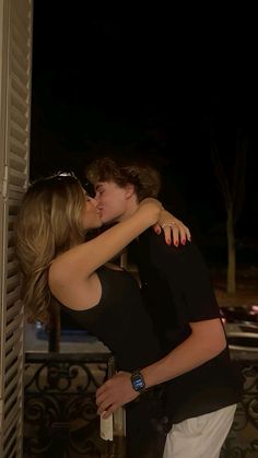 two people embracing each other in front of an open window at night with their arms around one another