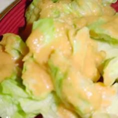 a red plate topped with lettuce covered in cheese and mustard dressing next to a fork